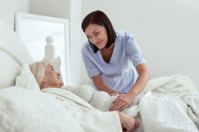 happy caregiver touching stomach while elder woman resting in bed